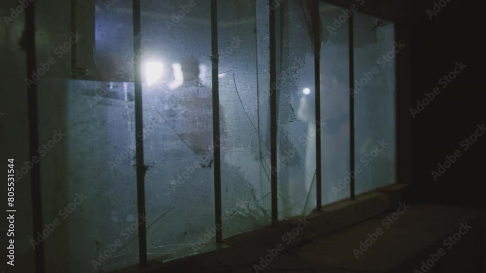 People wearing full protective suits and face masks and shining flashlights behind a broken window