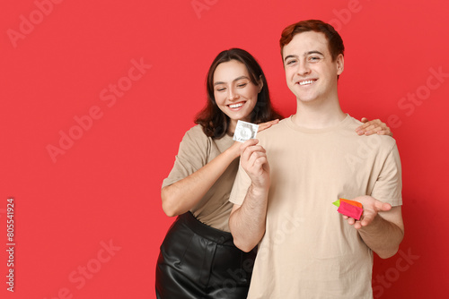 Young couple with condoms on red background. Safe sex concept