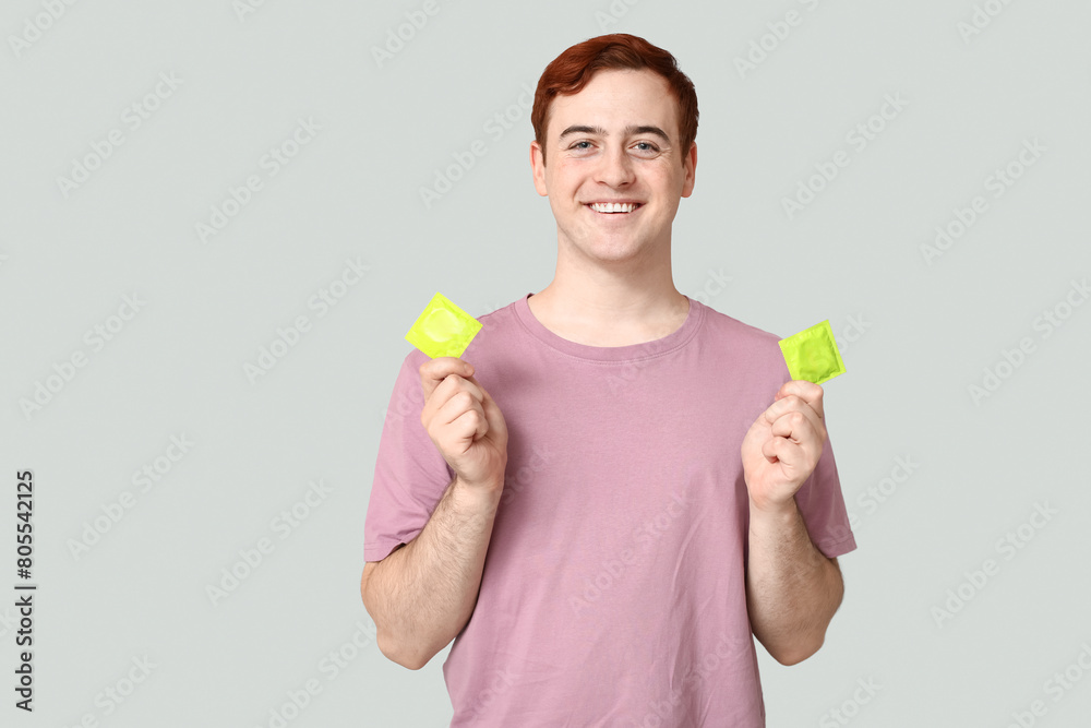 Young man with condoms on grey background. Safe sex concept Young man with condoms on grey background. Safe sex concept