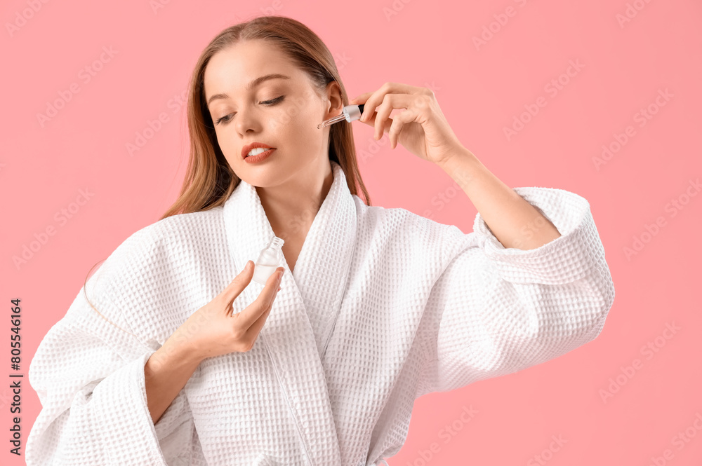 Young woman in bathrobe applying serum on pink background Young woman in bathrobe applying serum on pink background