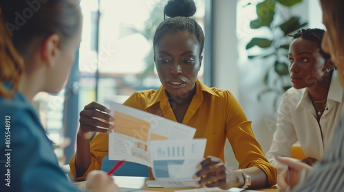 Black female project executive give printed handout materials to diverse teammates on meeting in office. Multiethnic staff group discuss sales result on briefing using paper reports with charts graphs photo