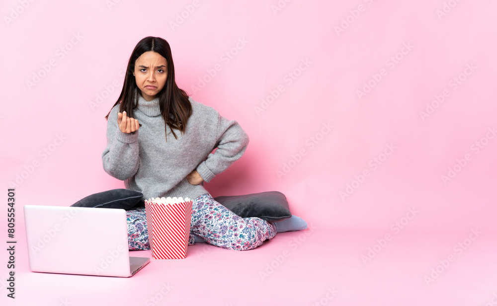 Young mixed race woman eating popcorn while watching a movie on the laptop making Italian gesture Young mixed race woman eating popcorn while watching a movie on the laptop making Italian gesture