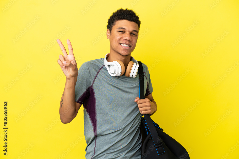Fototapeta premium Young sport African American man with sport bag isolated on yellow background smiling and showing victory sign