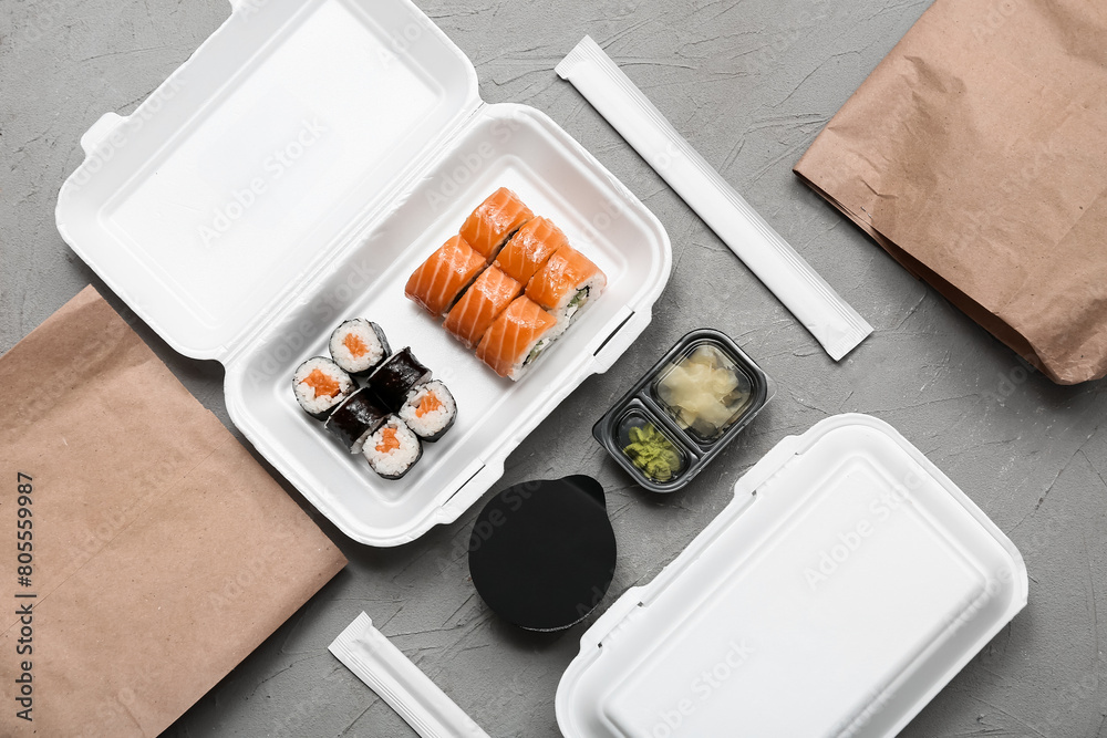 Plastic containers with tasty sushi rolls, chopsticks and paper bags on grey grunge background. Delivery concept Plastic containers with tasty sushi rolls, chopsticks and paper bags on grey grunge background. Delivery concept
