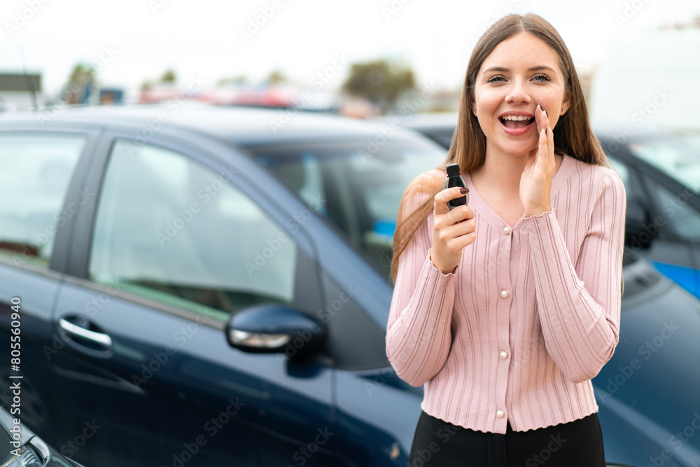 Young pretty blonde woman holding car keys at outdoors shouting with mouth wide open Young pretty blonde woman holding car keys at outdoors shouting with mouth wide open