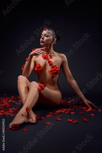 Passionate nude woman in petals surrounded by roses in dark studio