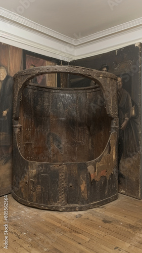 A large wooden barrel with a hole in the top is sitting in a room with a paintin