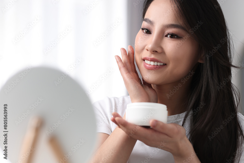 Happy woman applying face cream at home, space for text Happy woman applying face cream at home, space for text