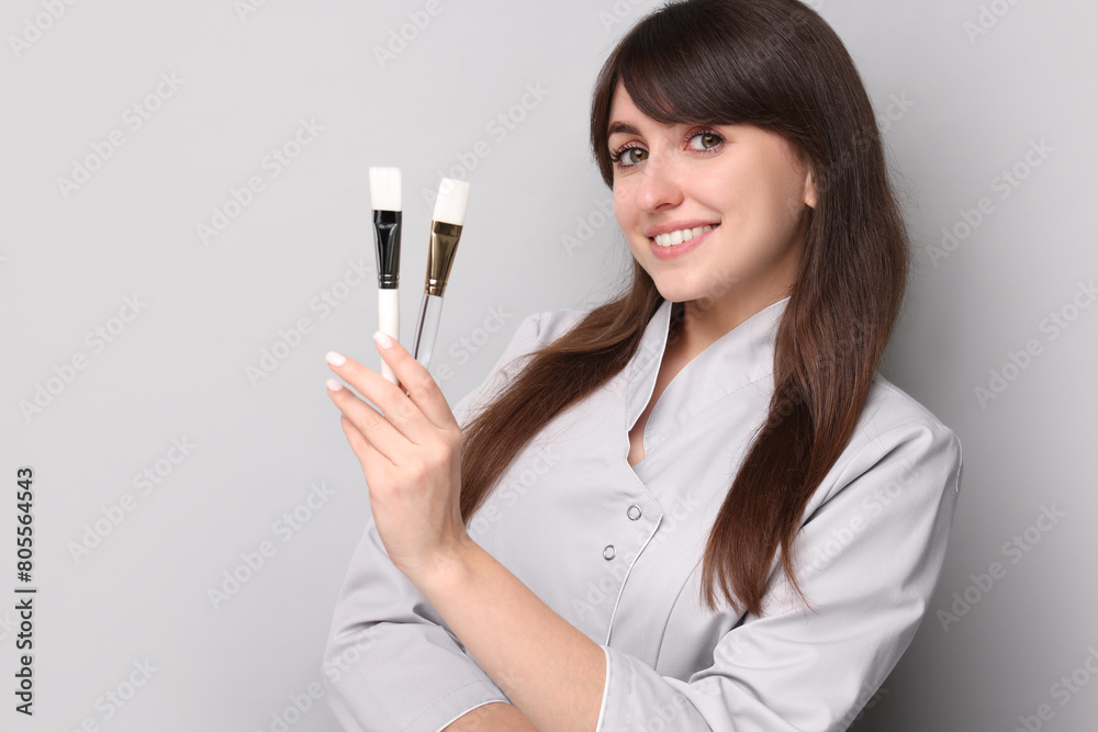 Cosmetologist with cosmetic brushes on grey background Cosmetologist with cosmetic brushes on grey background