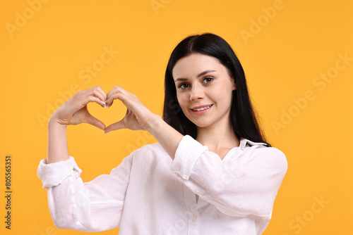 Foto Smiling woman showing heart gesture with hands on orange background