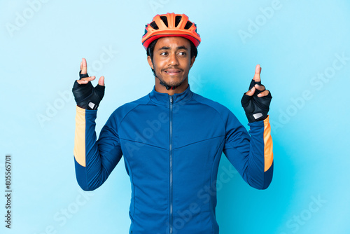 Young cyclist man with braids over isolated background with fingers crossing and wishing the best photo