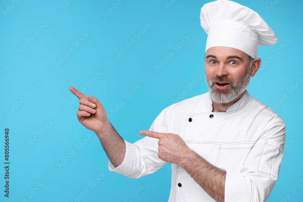 Surprised chef in uniform pointing at something on light blue background Surprised chef in uniform pointing at something on light blue background