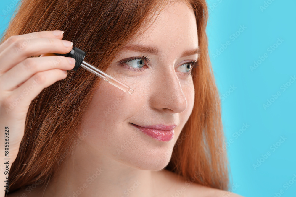 Beautiful woman with freckles applying cosmetic serum onto her face against light blue background, closeup Beautiful woman with freckles applying cosmetic serum onto her face against light blue background, closeup