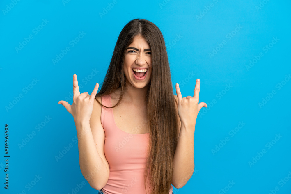 Fototapeta premium Young caucasian woman isolated on blue background making horn gesture