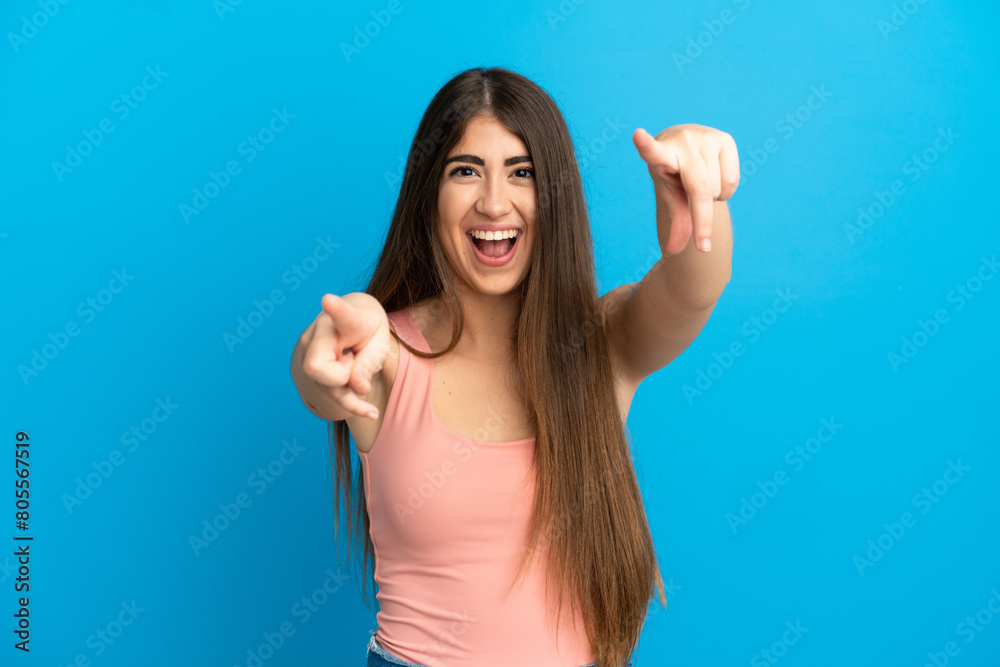 Fototapeta premium Young caucasian woman isolated on blue background surprised and pointing front