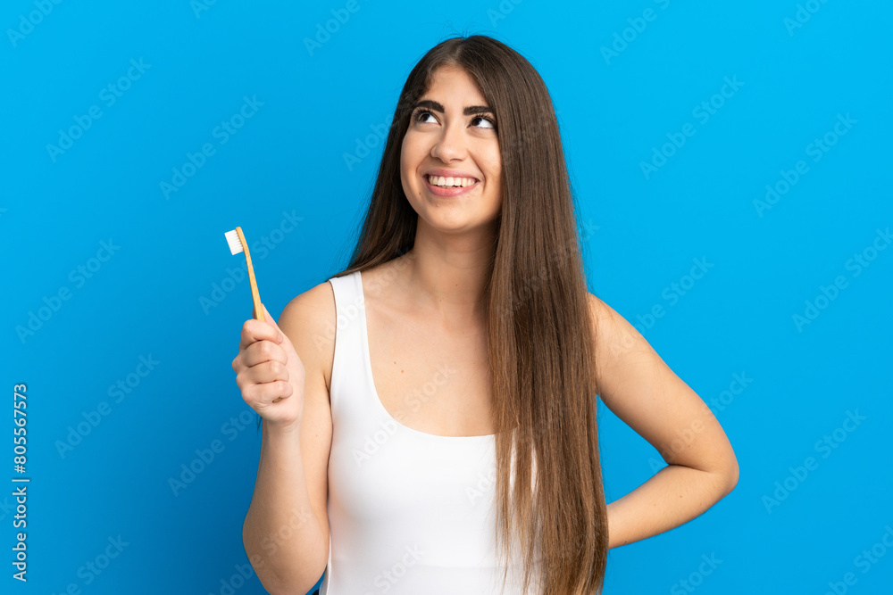 Young caucasian woman brushing teeth isolated on blue background thinking an idea while looking up Young caucasian woman brushing teeth isolated on blue background thinking an idea while looking up