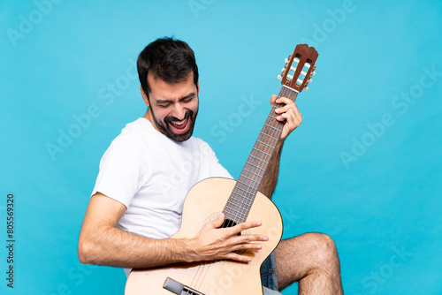 Young man with guitar over isolated blue background
