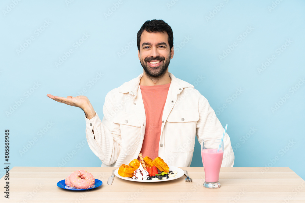 Man at a table having breakfast waffles and a milkshake holding copyspace imaginary on the palm to insert an ad Man at a table having breakfast waffles and a milkshake holding copyspace imaginary on the palm to insert an ad