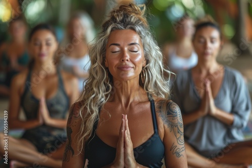 A focused yoga instructor with tattoos practices meditation with a group, presenting peace and harmony