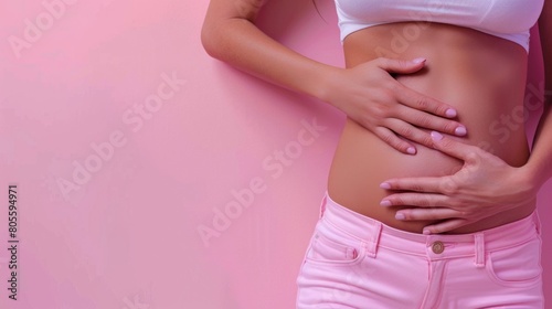Wallpaper Mural Close-up of a young woman in white top and pink pants touching her stomach gently on a soft pink background, portraying health and wellness. Torontodigital.ca