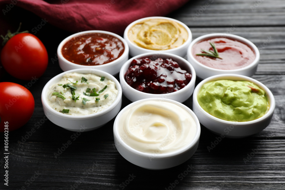 Different tasty sauces in bowls and tomatoes on black wooden table, closeup