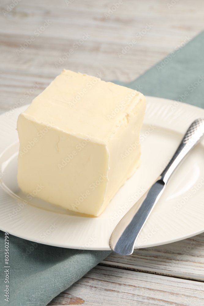 Block of tasty butter and knife on white wooden table