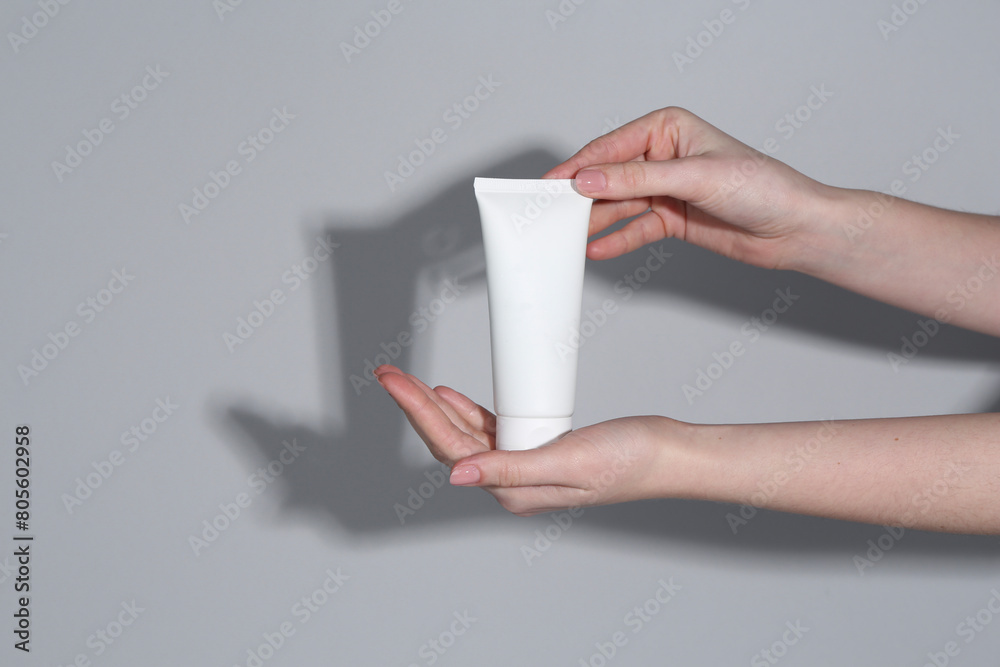 Woman holding tube of cream on grey background, closeup Woman holding tube of cream on grey background, closeup