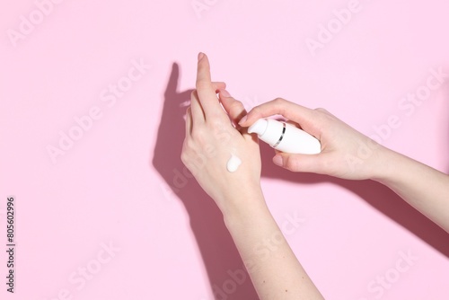 Woman applying cream on her hand against pink background, closeup