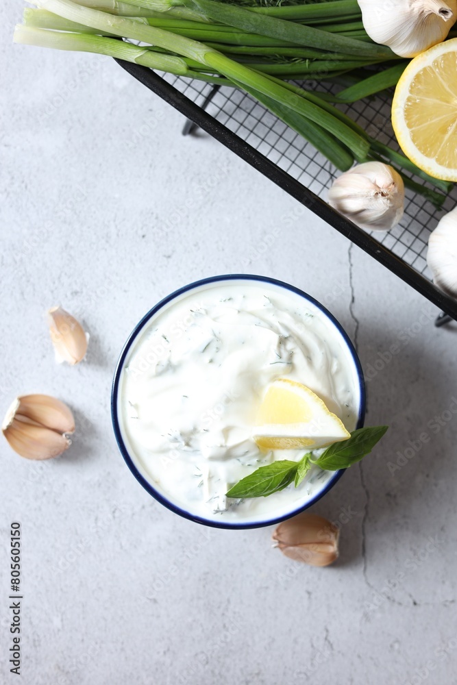 Delicious yogurt with dill in bowl, garlic, green onion and lemon on light textured table, flat lay
