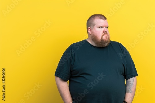 A man with a beard and a black shirt is standing in front of a yellow wall