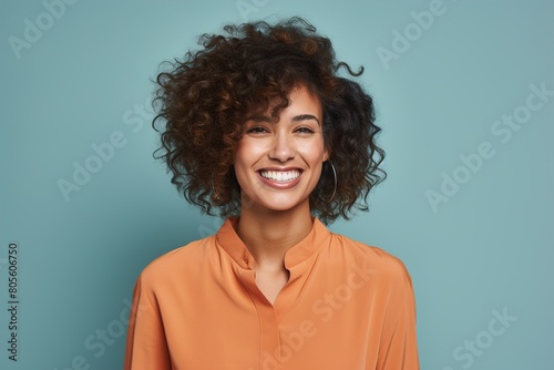 A woman with curly hair is smiling and wearing an orange shirt