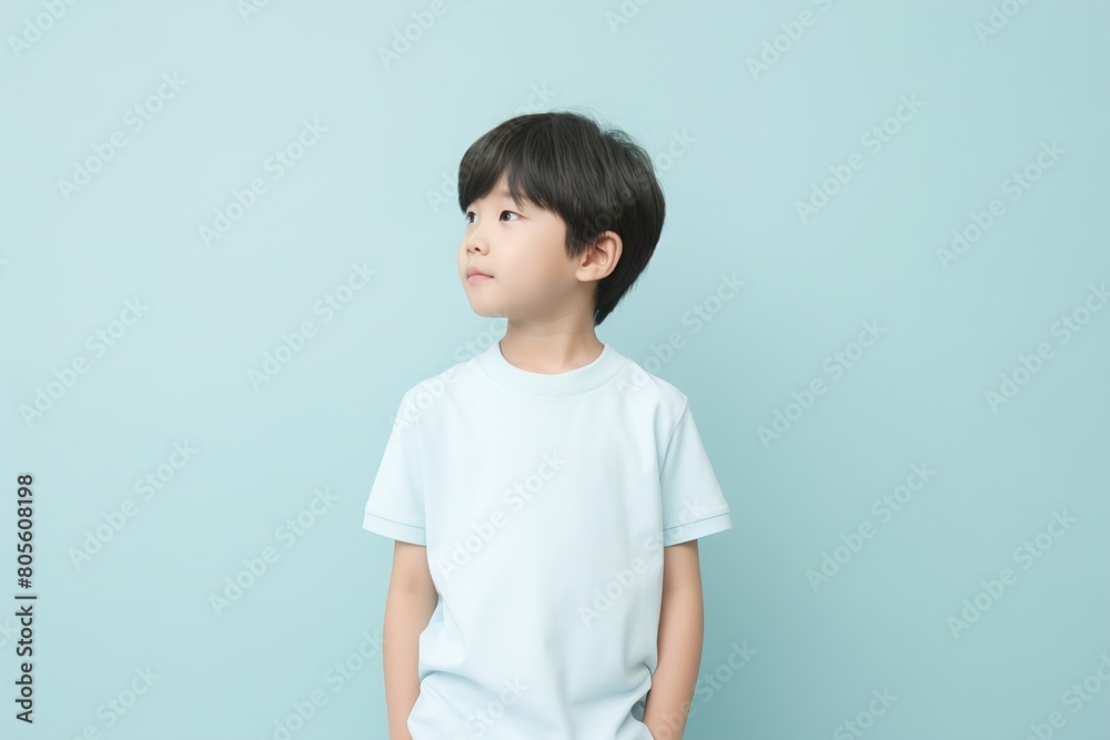 A young boy is standing in front of a blue wall, looking up at the ceiling A young boy is standing in front of a blue wall, looking up at the ceiling
