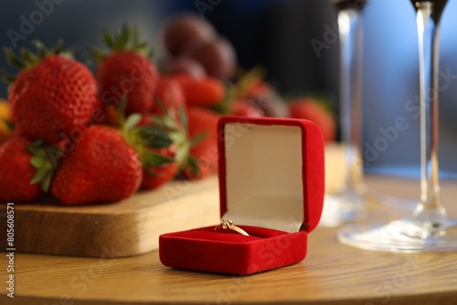 Engagement ring and fresh strawberries on wooden table, closeup. Romantic dinner