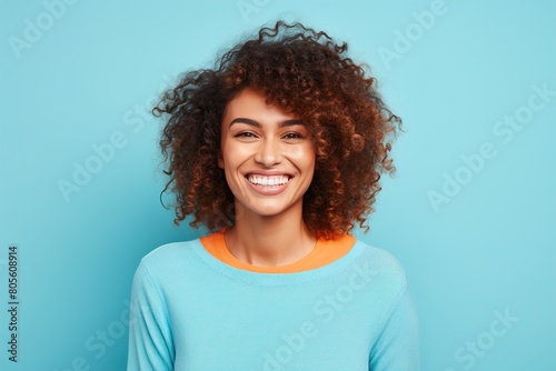 A woman with curly hair is smiling and wearing a blue sweater