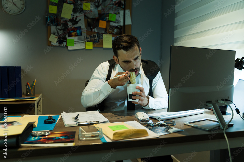 Detective eating takeout food while working on a case and looking at a computer screen at night Detective eating takeout food while working on a case and looking at a computer screen at night