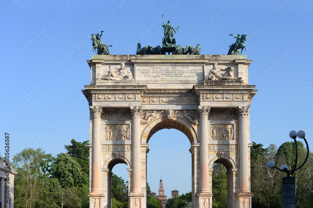 Fototapeta premium Porta Sempione with the Arco della Pace (arch of peace) triumphal arch and the towers of Castello Sforzeso (Sforza Castle) in the distance with blue sky on a late spring afternoon in Milan, Italy