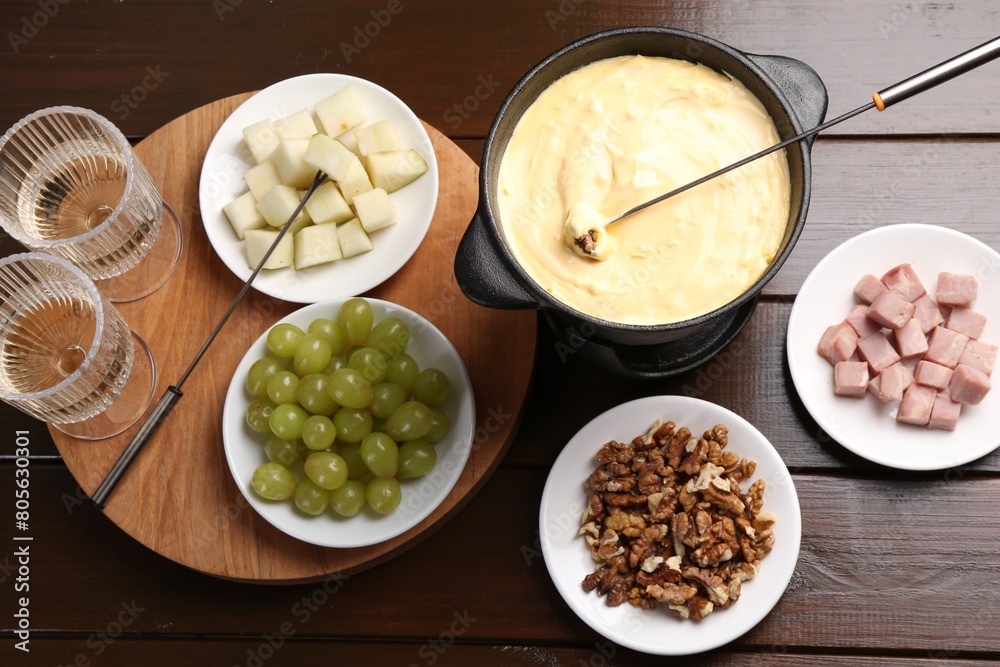 Fondue pot with tasty melted cheese, forks, wine and different snacks on wooden table, flat lay