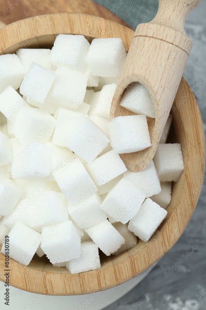 White sugar cubes in wooden bowl and scoop on grey table, top view White sugar cubes in wooden bowl and scoop on grey table, top view