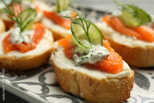 Tasty canapes with salmon, cucumber, cream cheese and dill on table, closeup