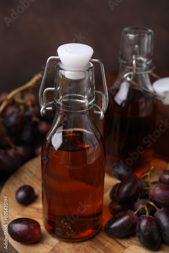 Bottles with wine vinegar and grapes on wooden table, closeup