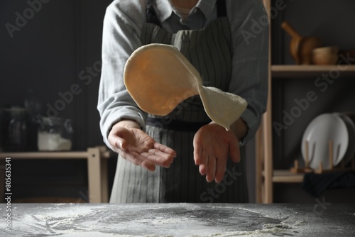 Woman tossing pizza dough at table in kitchen, closeup photo
