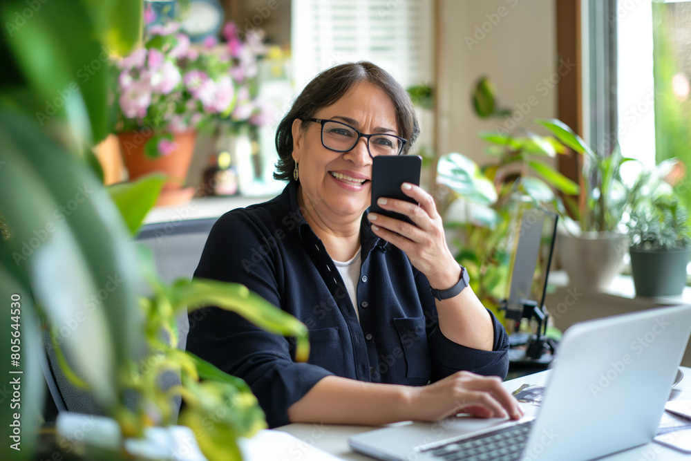 Joyful senior hispanic woman using smartphone at home office.