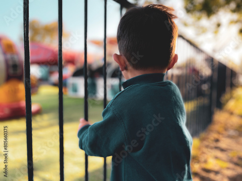 Young boy holding the railings behind a playground against a sunset sky