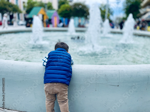 Little boy stands in front of a fountain against a cloudy day