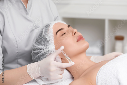 Professional cosmetologist holding skincare ampoule while working with client in clinic, closeup