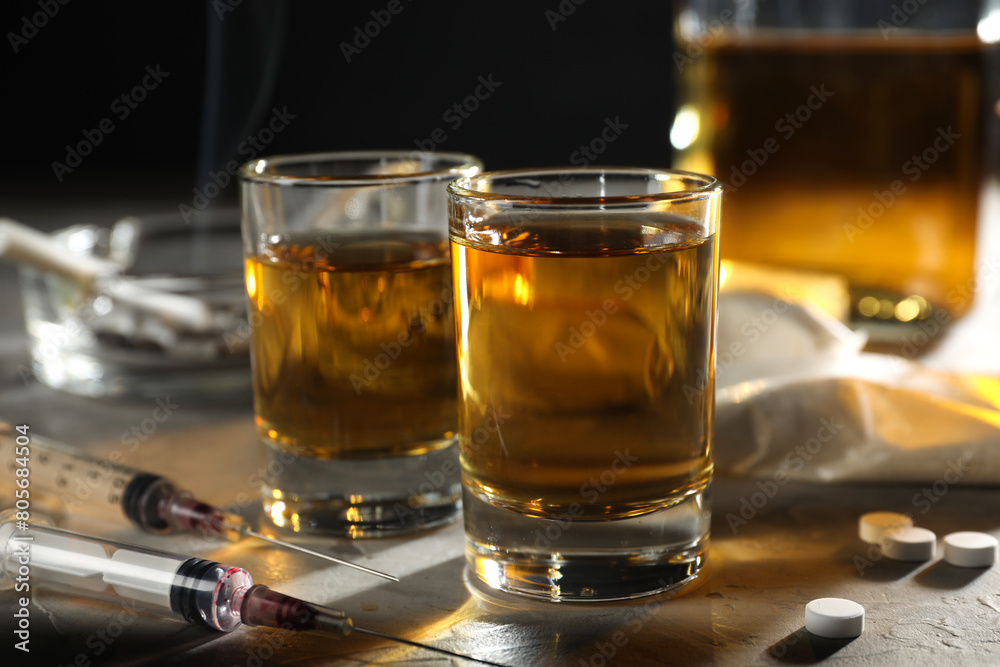 Alcohol and drug addiction. Whiskey in glasses, syringes and pills on grey background, closeup Alcohol and drug addiction. Whiskey in glasses, syringes and pills on grey background, closeup