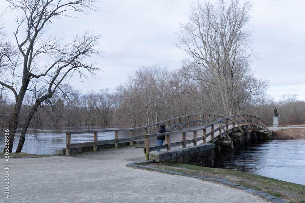 Old North bridge Minuteman National Park, Concord Massachusetts during spring flooding. A tourist standing on the bridge watching the flooding river flow.