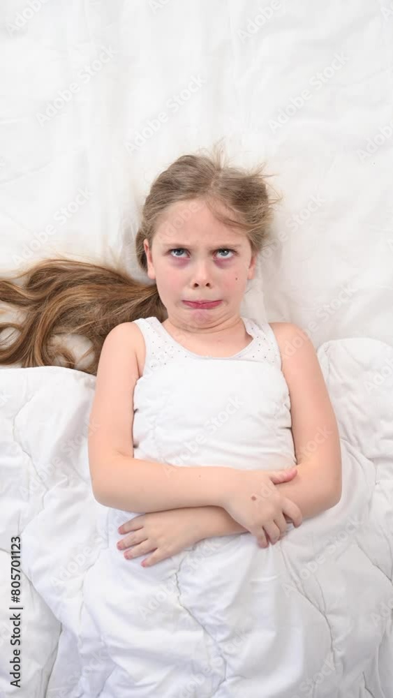 Top view of a little dissatisfied girl lying in bed. Vertical video. Top view of a little dissatisfied girl lying in bed. Vertical video.