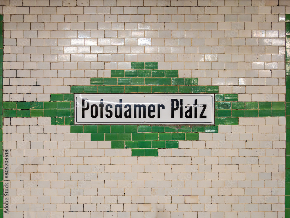 Fototapeta premium Potsdamer Platz station sign in Berlin. The location signage of the public transportation is part of the underground. The tiled wall is in white and green color.