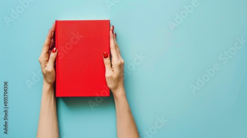 Woman's hands hold book with blank red cover, light blue background. Ai Generated